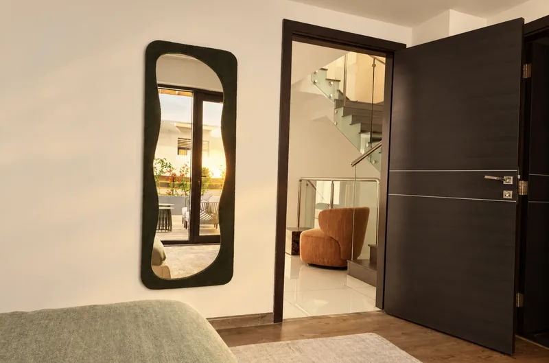 Dunia bedroom with green wavy mirror and open door to the glass-railed staircase landing