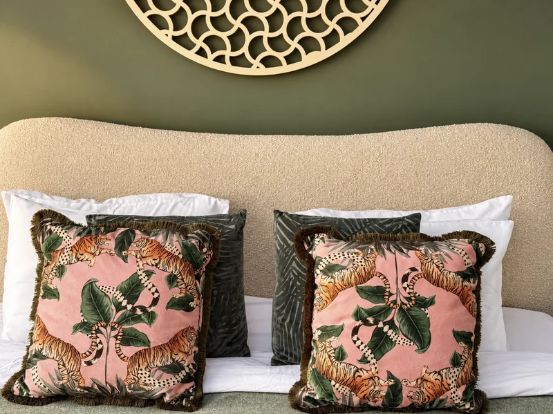 Pink tiger-print cushions on a boucle headboard beneath a carved round wall panel
