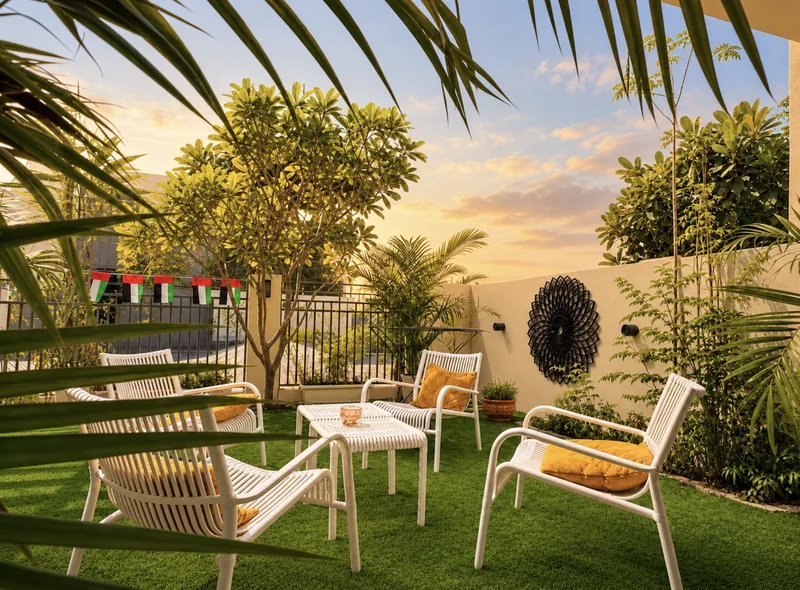 Dunia garden lounge with white chairs and yellow cushions on artificial grass, palms and UAE flag bunting