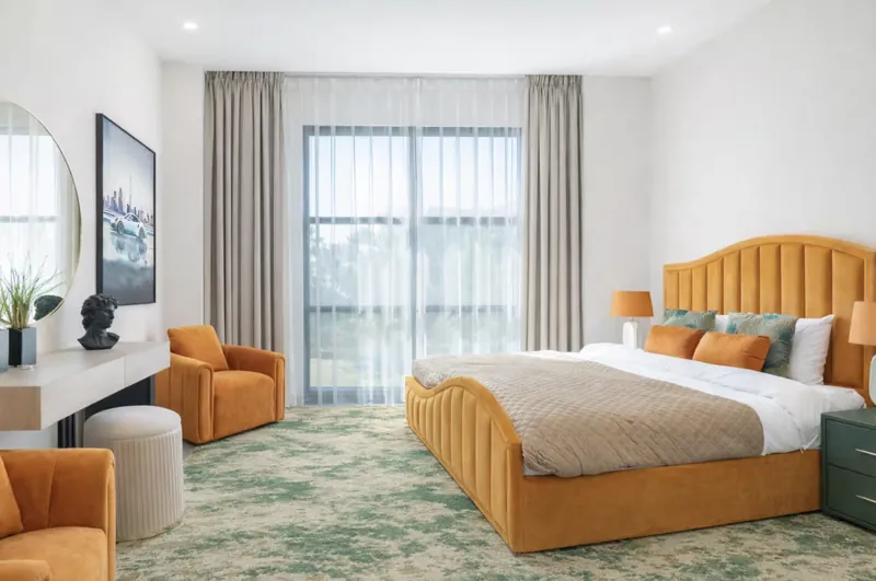 Bedroom with orange velvet bed and armchairs and a green patterned rug