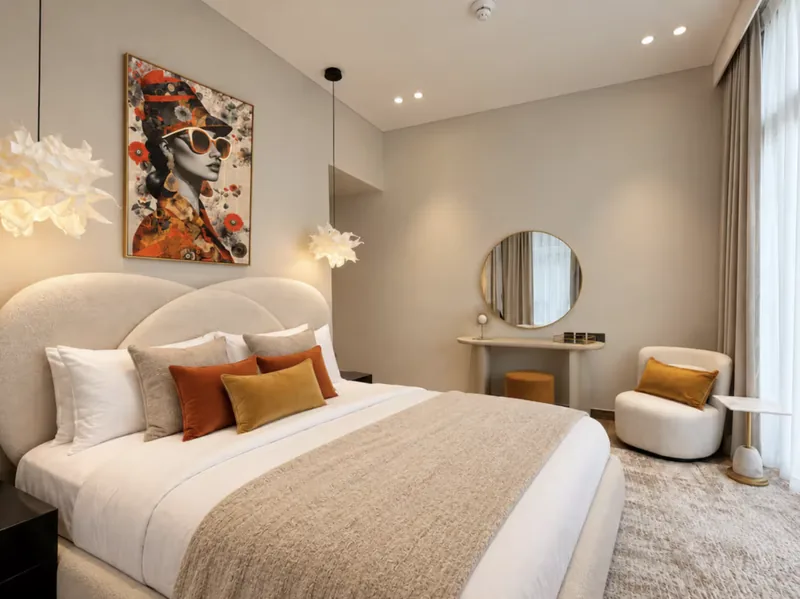 Mirage bedroom with curved cream headboard, orange cushions, pop-art portrait and vanity with round mirror