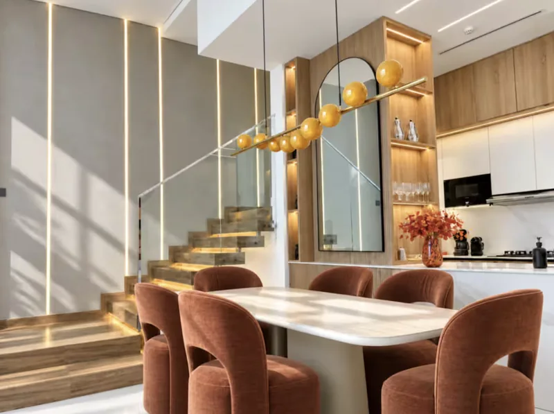 Mirage dining table with rust velvet chairs and gold globe pendant, beside the floating staircase and kitchen