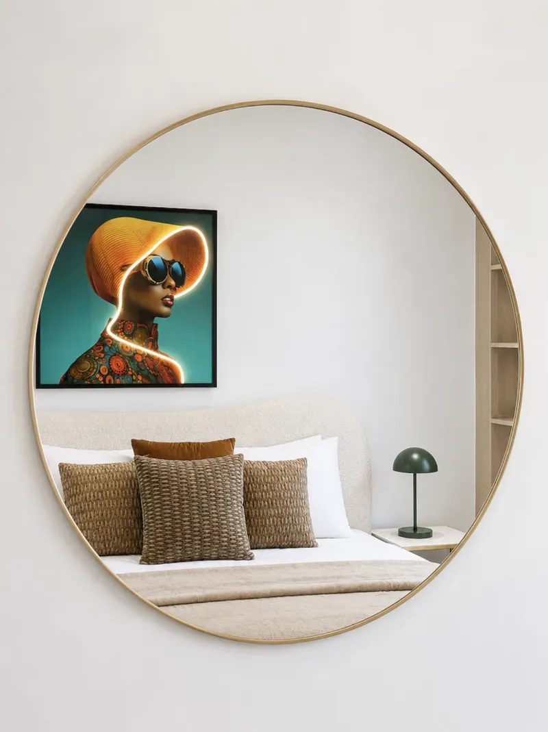 Round brass mirror reflecting the bed, woven cushions and neon portrait artwork in a ParkView bedroom