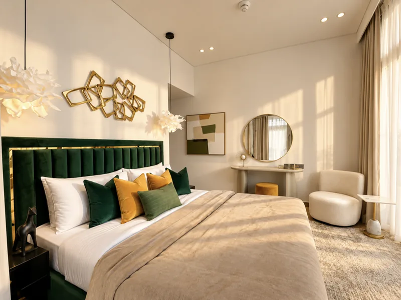 Pearl bedroom with emerald velvet headboard, gold geometric wall art, vanity and mustard ottoman