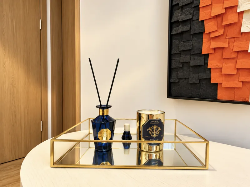 Gold-framed mirrored tray with navy reed diffuser and gold candle on a white table